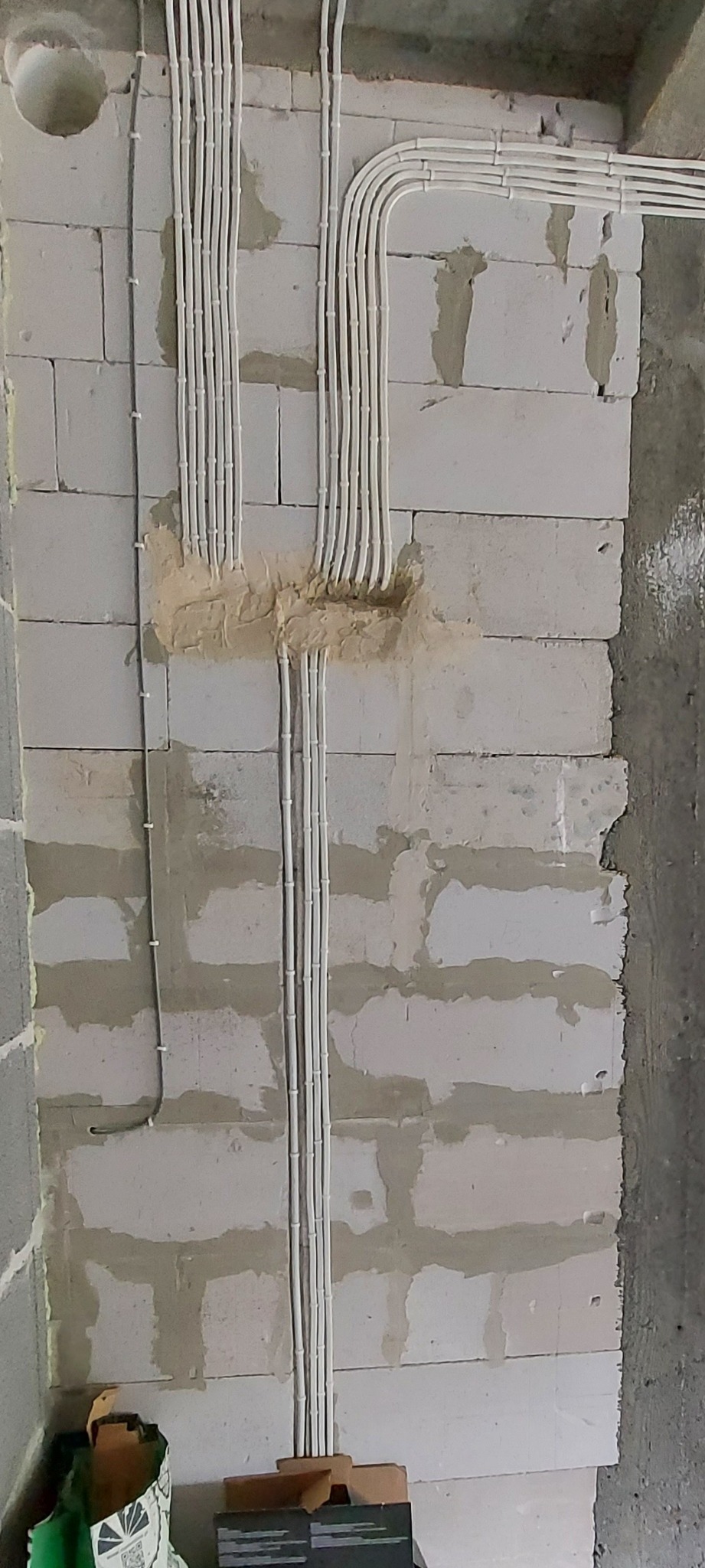 Ściana z betonu komórkowego z widocznymi przewodami elektrycznymi ułożonymi w peszlach, częściowo zamaskowanymi gipsem.