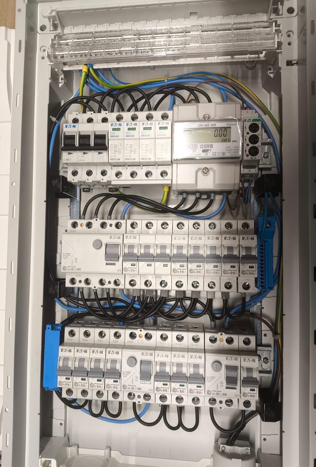 Rozdzielnica elektryczna Eaton z zamontowanymi bezpiecznikami, przewodami i licznikiem energii elektrycznej. Widok z bliska na kompletną instalację w skrzynce.