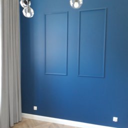 1. MARCUS BUDOWNICTWO I REMONTY WOJCIECH ZWARA - Ściana pomalowana na ciemny odcień niebieskiego z dwoma prostokątnymi, wpuszczonymi panelami dekoracyjnymi, parkiet w jodełkę, nowoczesna lampa sufitowa z kulistymi kloszami, szare zasłony...