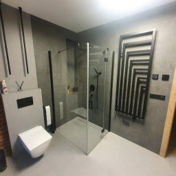 1. MARCUS BUDOWNICTWO I REMONTY WOJCIECH ZWARA - Nowoczesna łazienka w szarościach z kabiną prysznicową typu walk-in, wiszącą toaletą i grzejnikiem dekoracyjnym. Widoczna ściana z cegły i minimalistyczne dodatki.