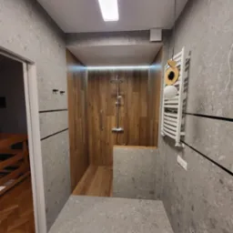 Nowoczesna kabina prysznicowa walk-in z drewnianą okładziną, szarymi płytkami imitującymi kamień, grzejnikiem drabinkowym i oświetleniem LED.