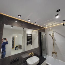 VIKTOR PRODANIUK VIKTORLUXPRO - Nowoczesna łazienka z marmurowymi płytkami, złotą armaturą i podświetlanym lustrem, widok na kabinę prysznicową i grzejnik drabinkowy, odbicie osoby robiącej zdjęcie.