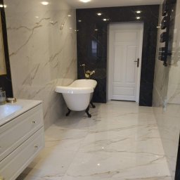 Best- Fliz Katowice - Elegancka łazienka z wolnostojącą wanną na lwich nóżkach, marmurowe płytki w odcieniach bieli i złota, czarne akcenty płytek i grzejnika drabinkowego, oświetlenie punktowe.