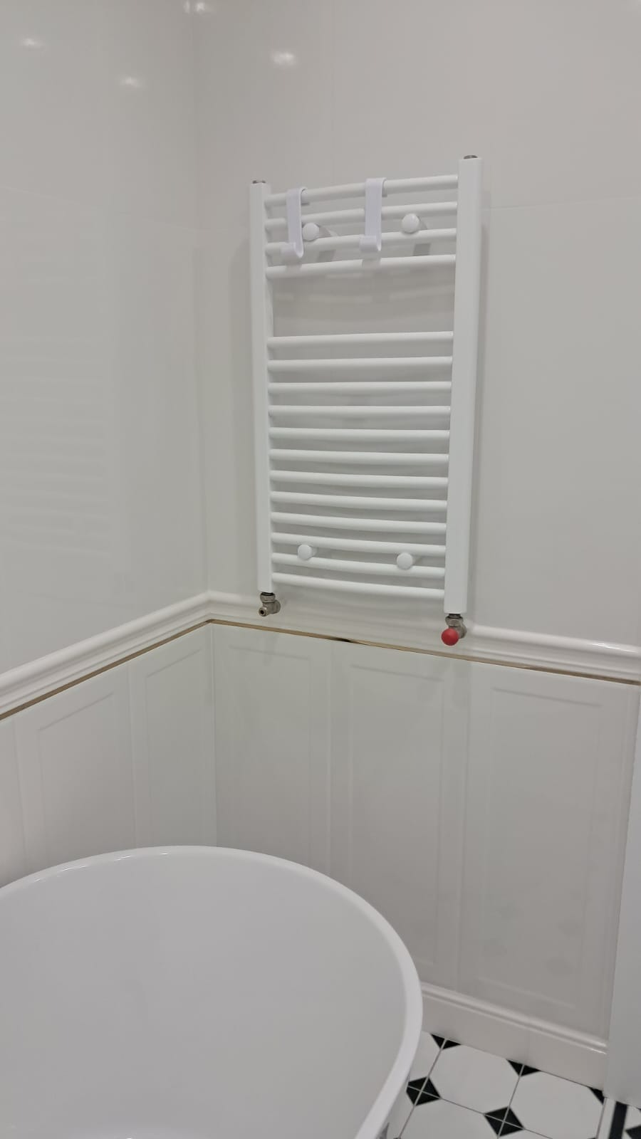 Biała łazienka z grzejnikiem drabinkowym, panelami ściennymi i fragmentem owalnej wanny.