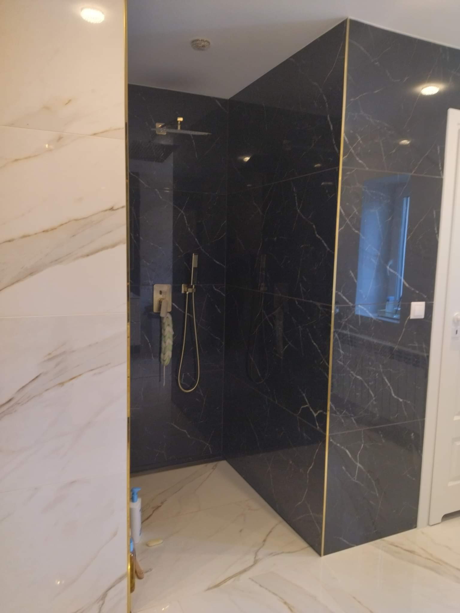 Wykończona kabina prysznicowa w Katowicach z czarnymi płytkami imitującymi marmur z złotymi listwami, kontrastująca z białymi płytkami na ścianie obok.