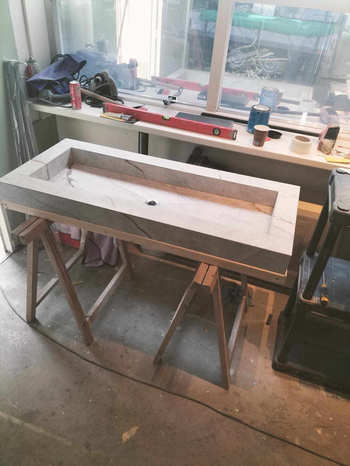 Montaż umywalki z jasnego marmuru na drewnianych kozłach w warsztacie, widoczne narzędzia i akcesoria na parapecie okiennym.