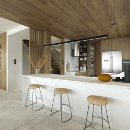 MODELOVE STUDIO - Nowoczesna kuchnia z wyspą wykończoną marmurem, drewniany sufit, oświetlenie liniowe LED, minimalistyczne krzesła barowe z drewnianymi siedziskami, dekoracyjna dynia na blacie.