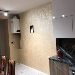 SVBUD Vasyl Stefaniuk - Beżowa ściana z dekoracyjną fakturą w wyremontowanej kuchni, widoczny piec gazowy, marmurowe płytki podłogowe i fragment zabudowy kuchennej