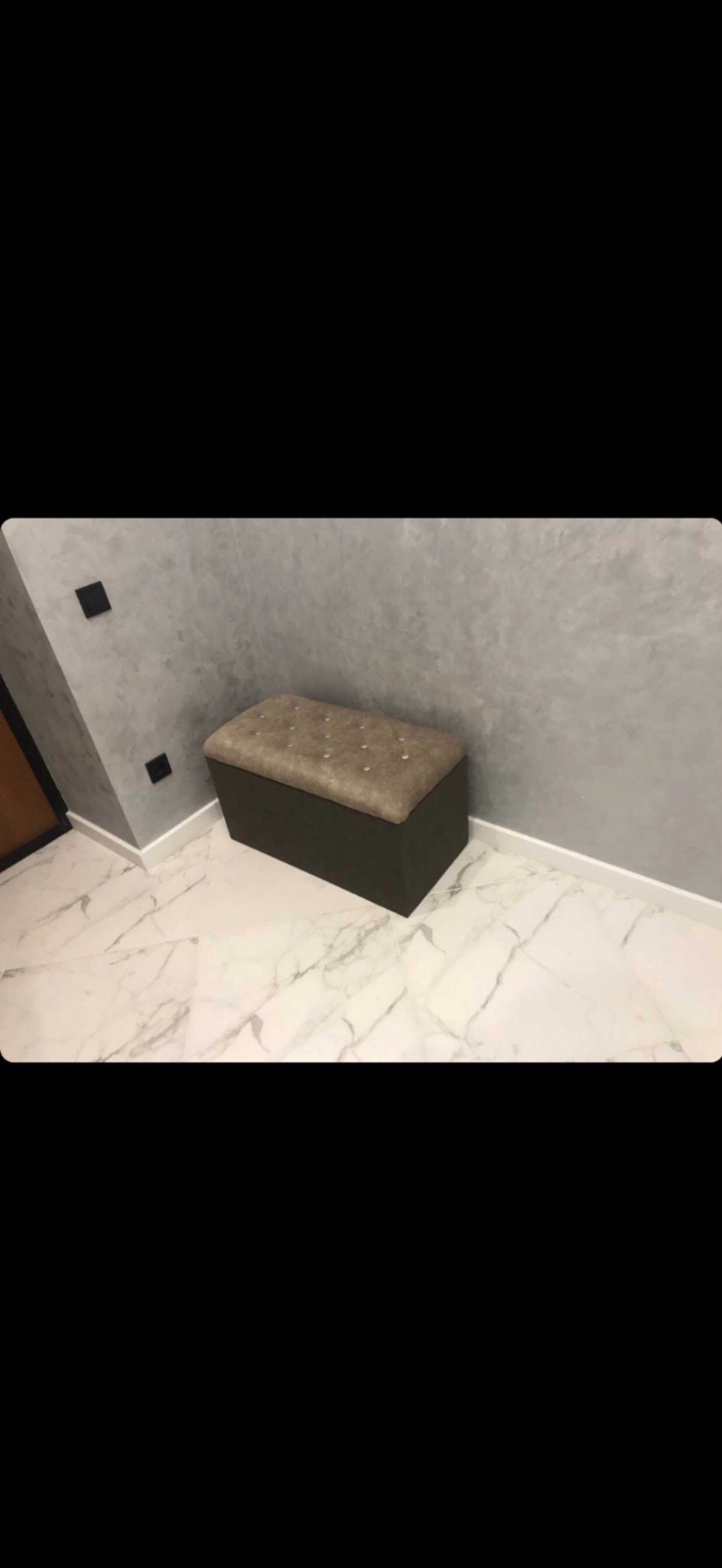 Szary, teksturowany efekt na ścianie w korytarzu z marmurową podłogą i ciemnobrązową pufą z tapicerowanym siedziskiem.