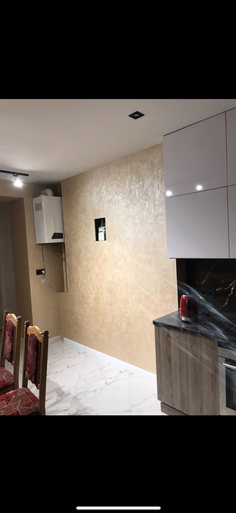 Beżowa ściana z dekoracyjną fakturą w wyremontowanej kuchni, widoczny piec gazowy, marmurowe płytki podłogowe i fragment zabudowy kuchennej