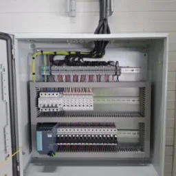 Otwarta szafa sterownicza z precyzyjnie ułożonymi przewodami i modułami. Widoczne listwy zaciskowe, bezpieczniki i zasilacz. Estetyczne i profesjonalne wykonanie instalacji elektrycznej.