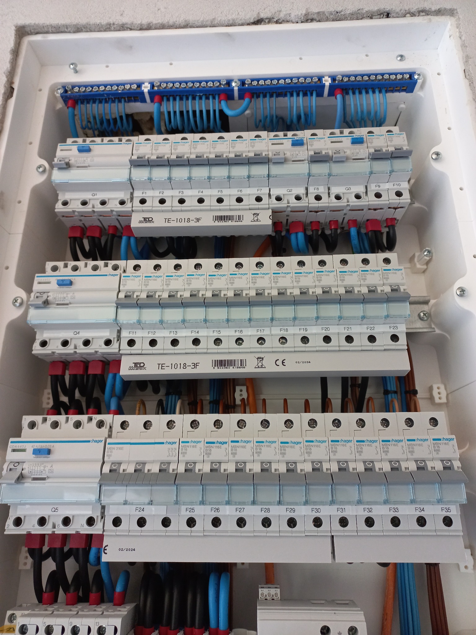 Rozdzielnica elektryczna Hager z zainstalowanymi bezpiecznikami i okablowaniem. Widoczne oznaczenia i numery obwodów. Instalacja w białej obudowie.