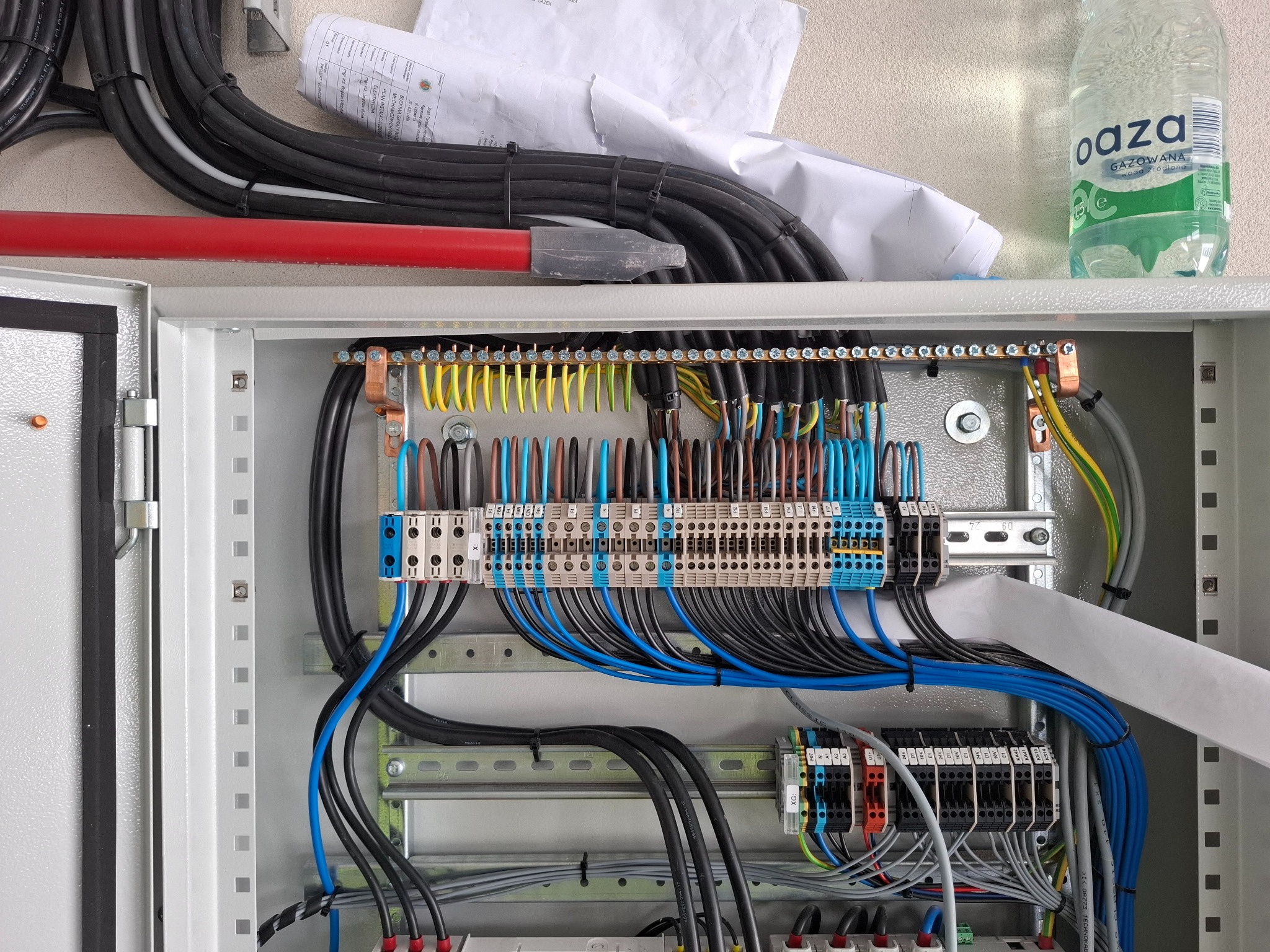 Rozdzielnica elektryczna z precyzyjnie ułożonymi przewodami w kolorach: czarnym, niebieskim, żółto-zielonym. Widoczne zabezpieczenia i listwy zaciskowe.