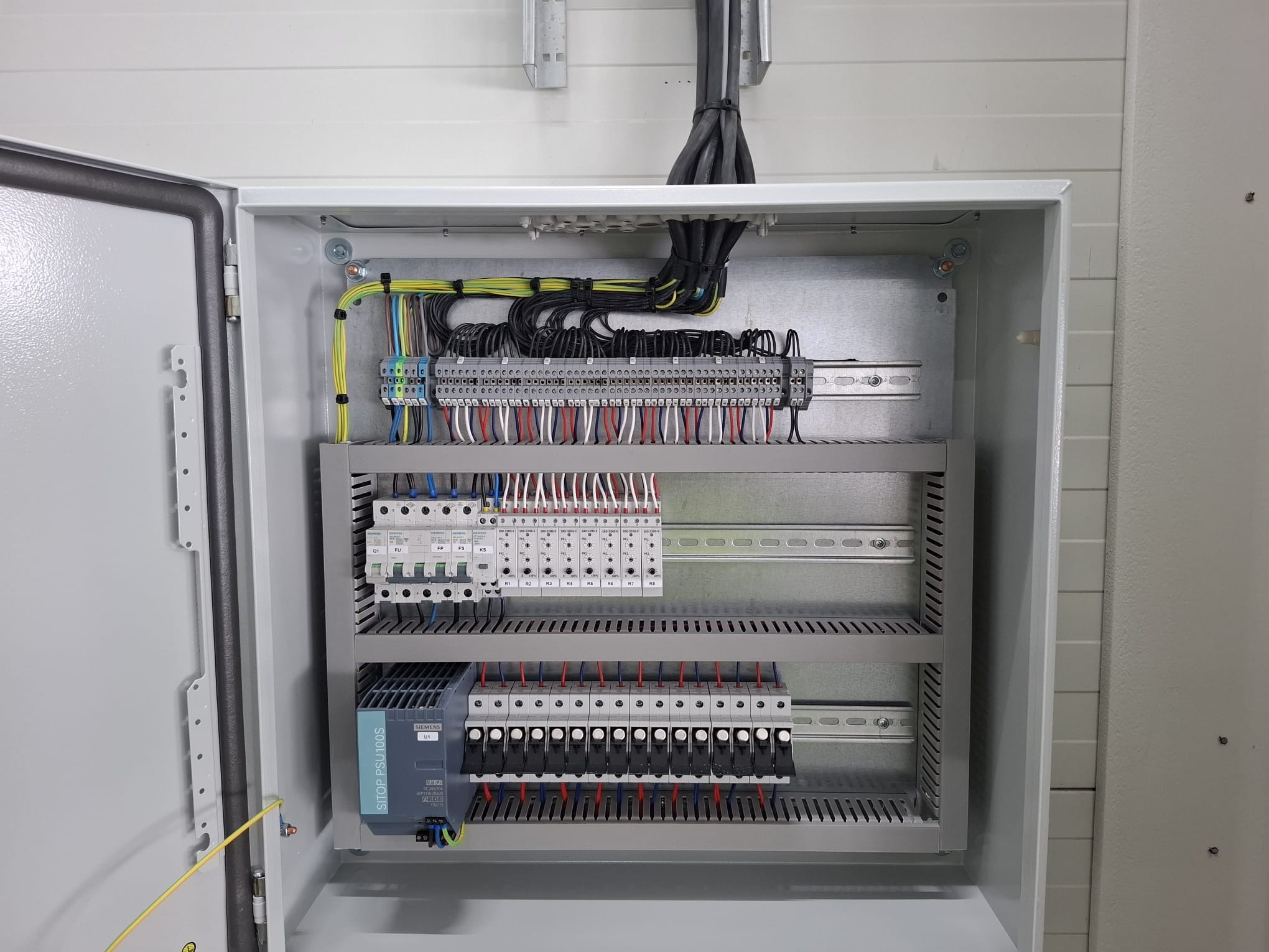 Otwarta szafa sterownicza z precyzyjnie ułożonymi przewodami i modułami. Widoczne listwy zaciskowe, bezpieczniki i zasilacz. Estetyczne i profesjonalne wykonanie instalacji elektrycznej.