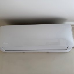 HYDROLINE SPÓŁKA Z OGRANICZONĄ ODPOWIEDZIALNOŚCIĄ - Biała klimatyzacja Rotenso Imoto Series zamontowana na beżowej ścianie w pomieszczeniu. Widoczne przewody instalacyjne.