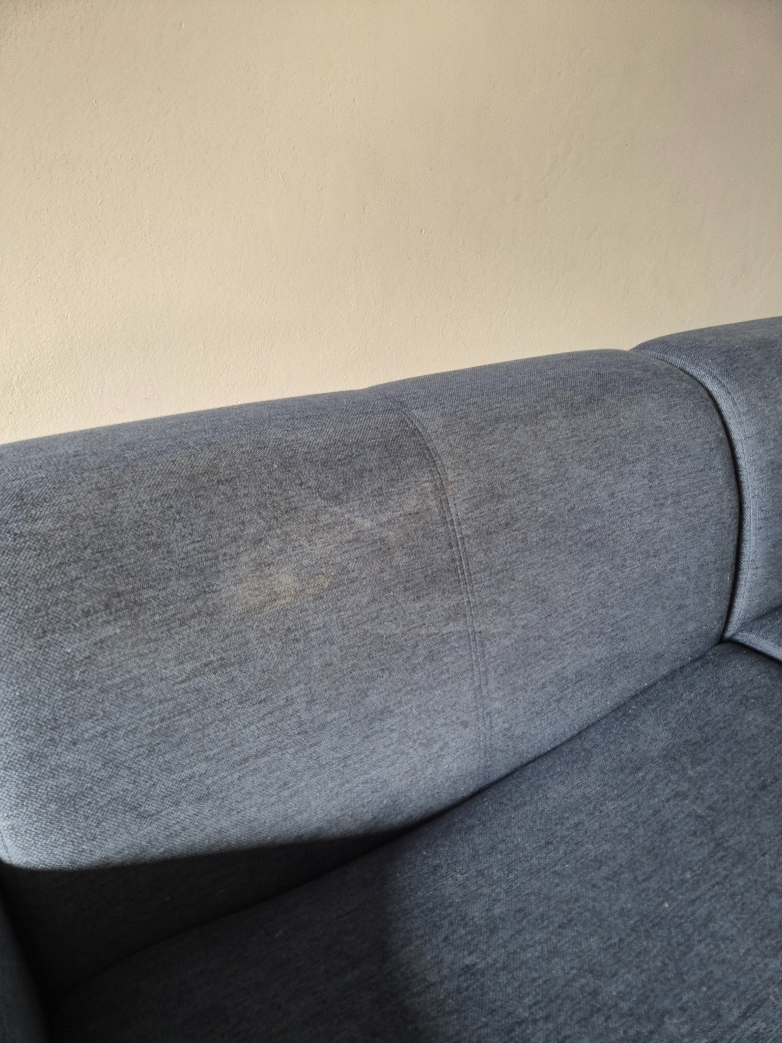 Szara kanapa z widocznymi plamami na oparciu, na tle beżowej ściany.