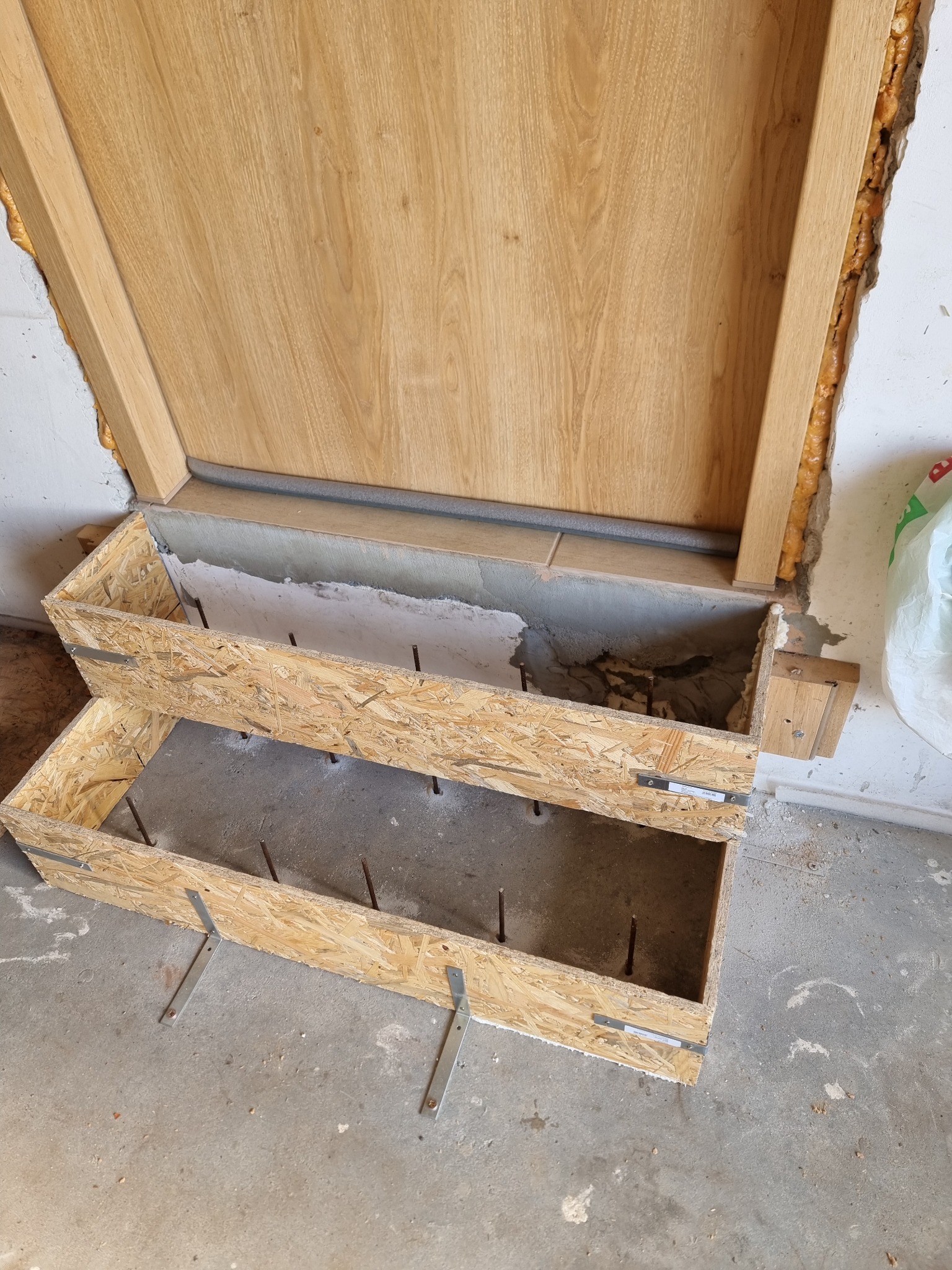 Przygotowanie podłoża pod schody z drewnianą ramą i wystającymi prętami zbrojeniowymi, widoczne płyty OSB i pianka montażowa.