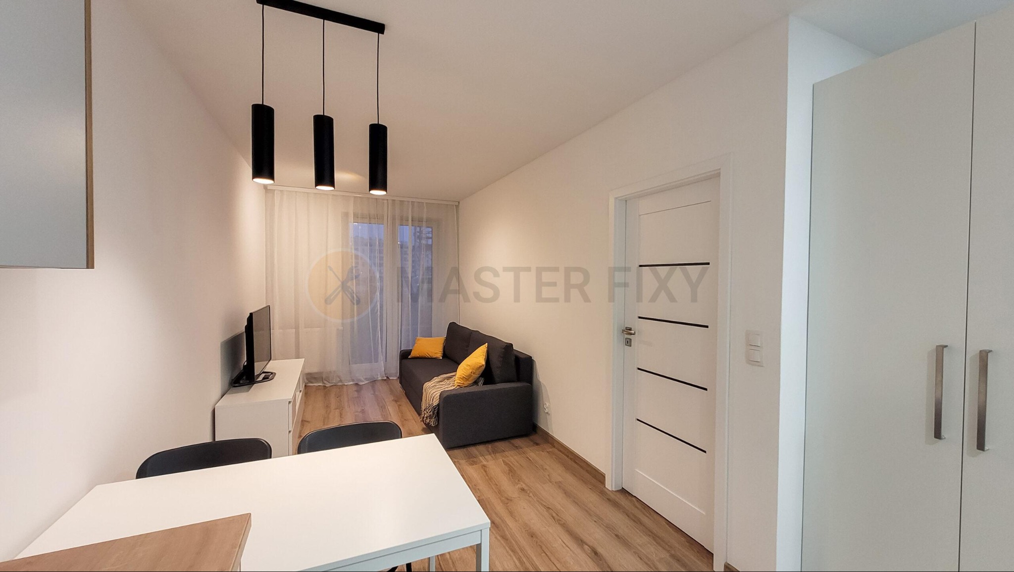 Jasne wnętrze salonu z drewnianą podłogą, szarą sofą z żółtymi poduszkami, białym stołem i szafą, oświetlone trzema czarnymi lampami wiszącymi.