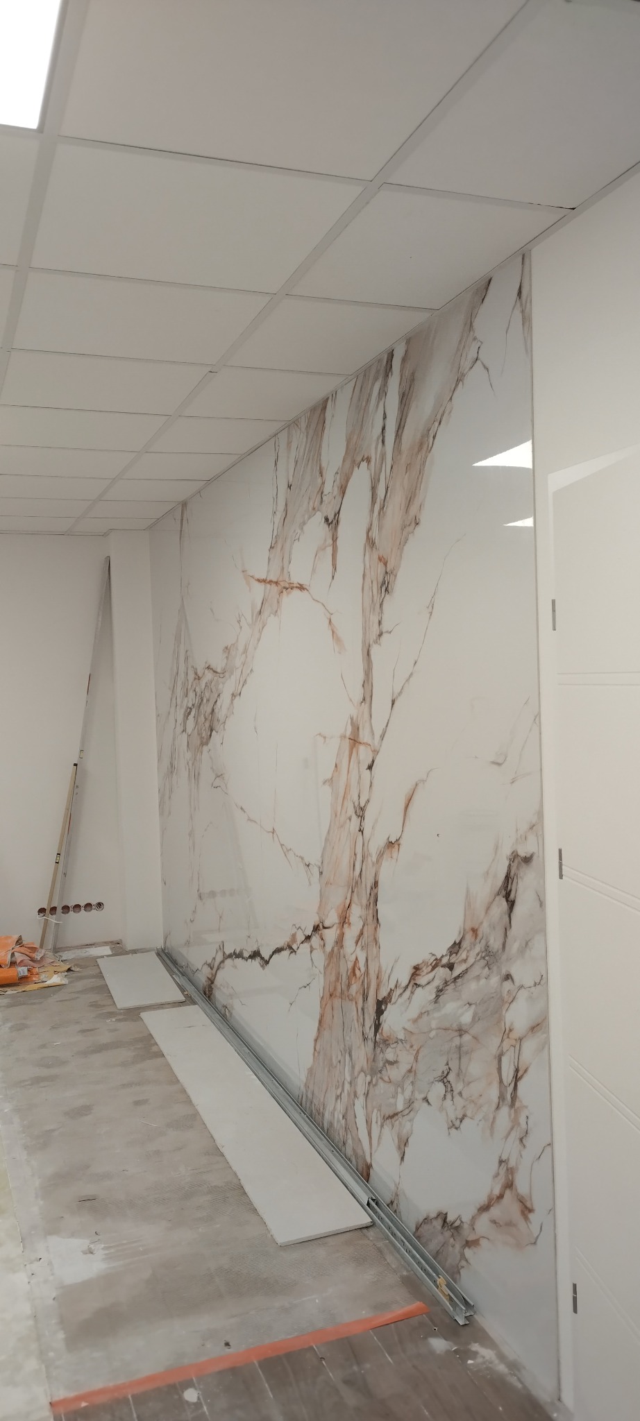 Montaż dekoracyjnych paneli ściennych imitujących marmur w jasnym wnętrzu. Widoczne profile montażowe i drabina malarska. Nowoczesny design.