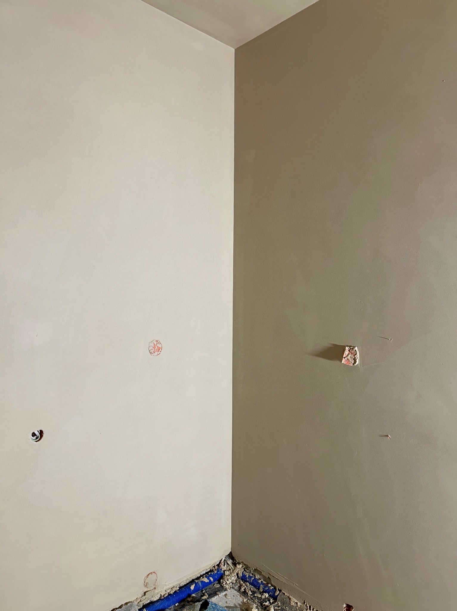 Świeżo nałożony, gładki tynk maszynowy w rogu pomieszczenia, widoczne instalacje elektryczne i rury w podłodze, przygotowane do dalszych prac wykończeniowych.
