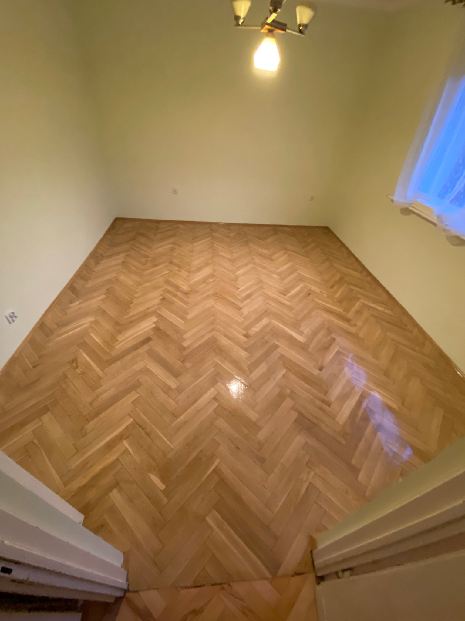 Parkiet ułożony w jodełkę na podłodze w pokoju, widok z góry, lampa sufitowa w tle.