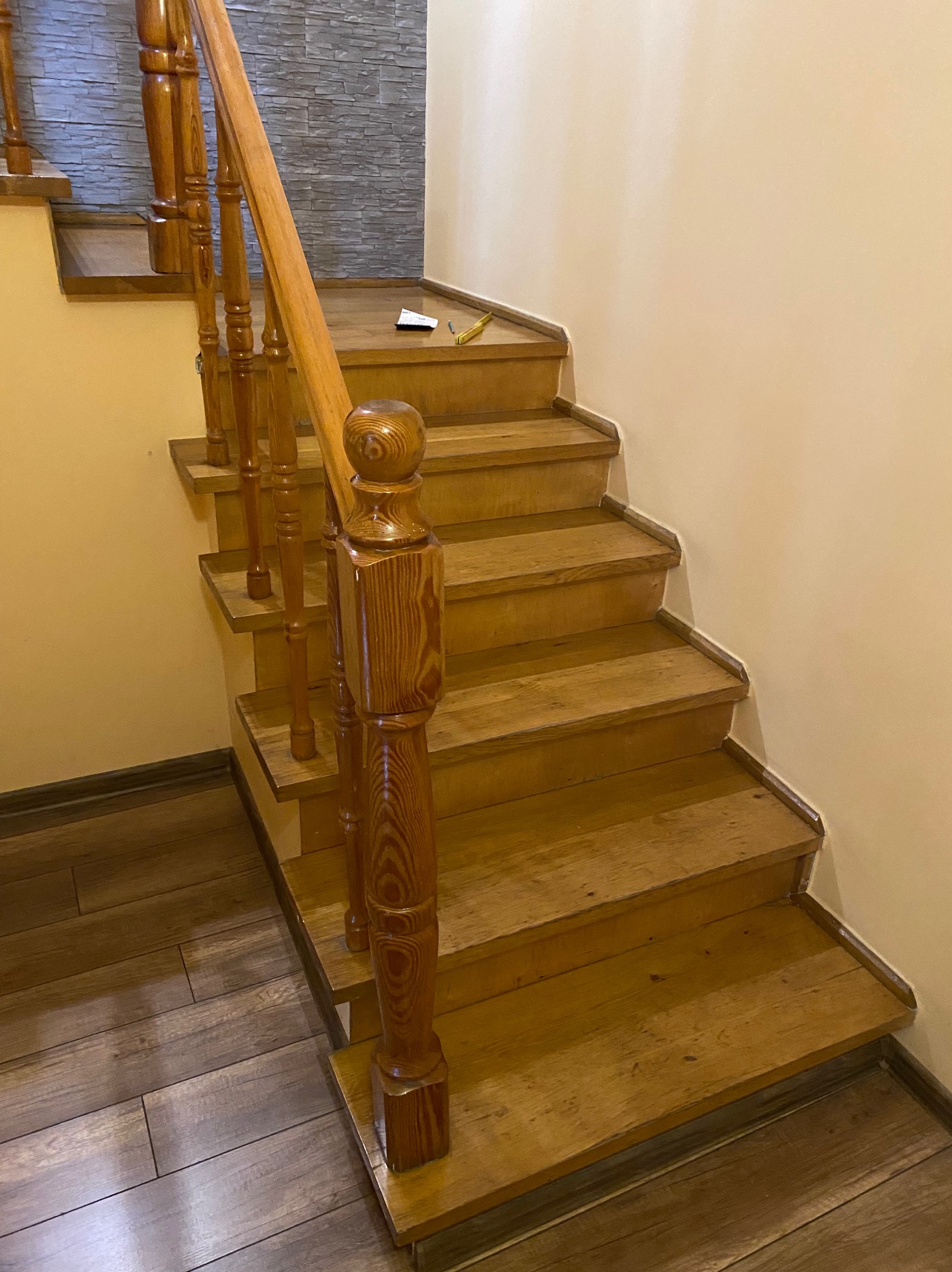 Drewniane schody z balustradą po renowacji, widoczne ślady po szlifowaniu i lakierowaniu, na górnym stopniu leży ołówek i kartka.