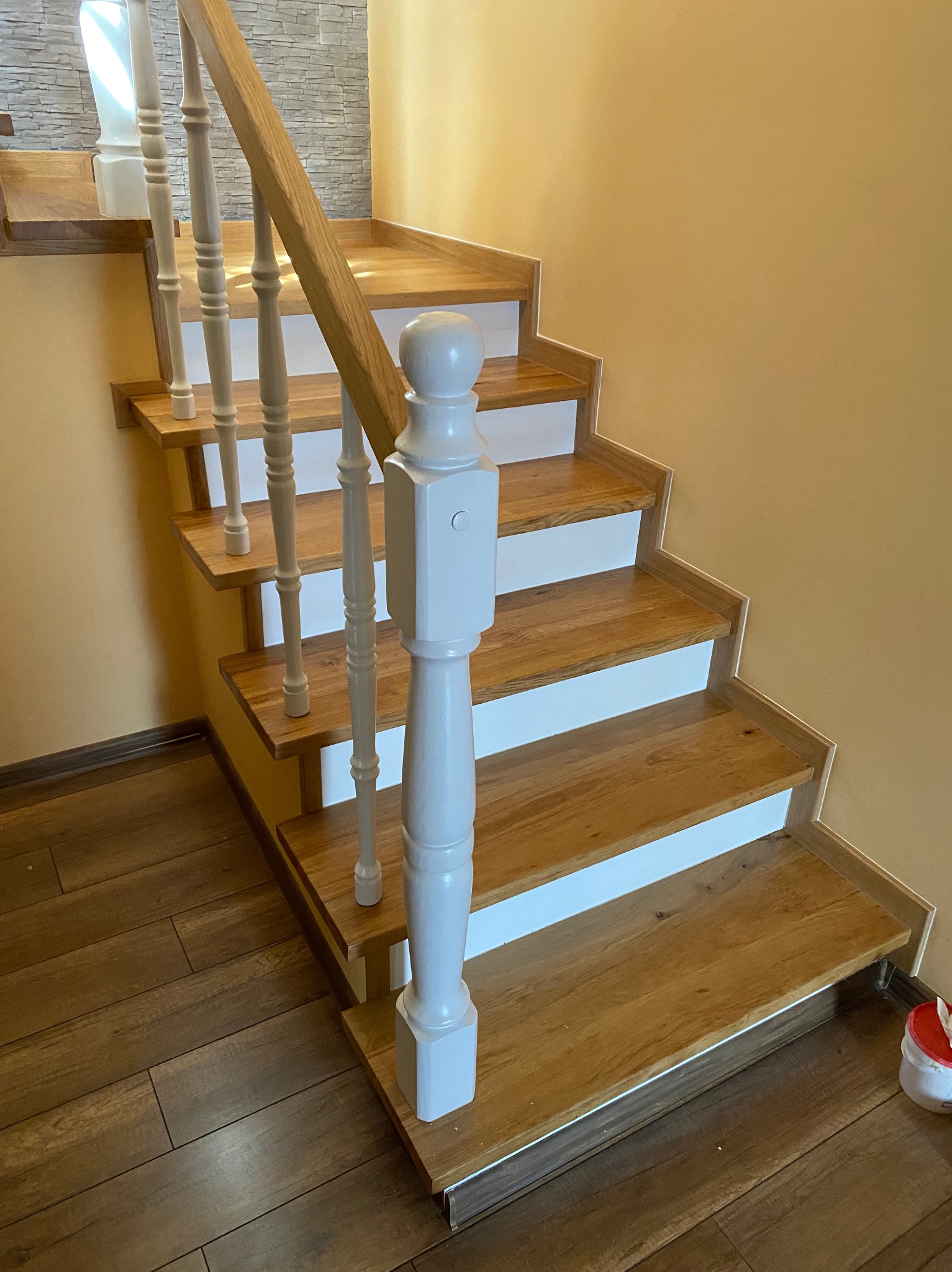 Odnowione drewniane schody z białymi podstopnicami i jasnoszarymi balustradami, widok z dołu na pierwsze stopnie.