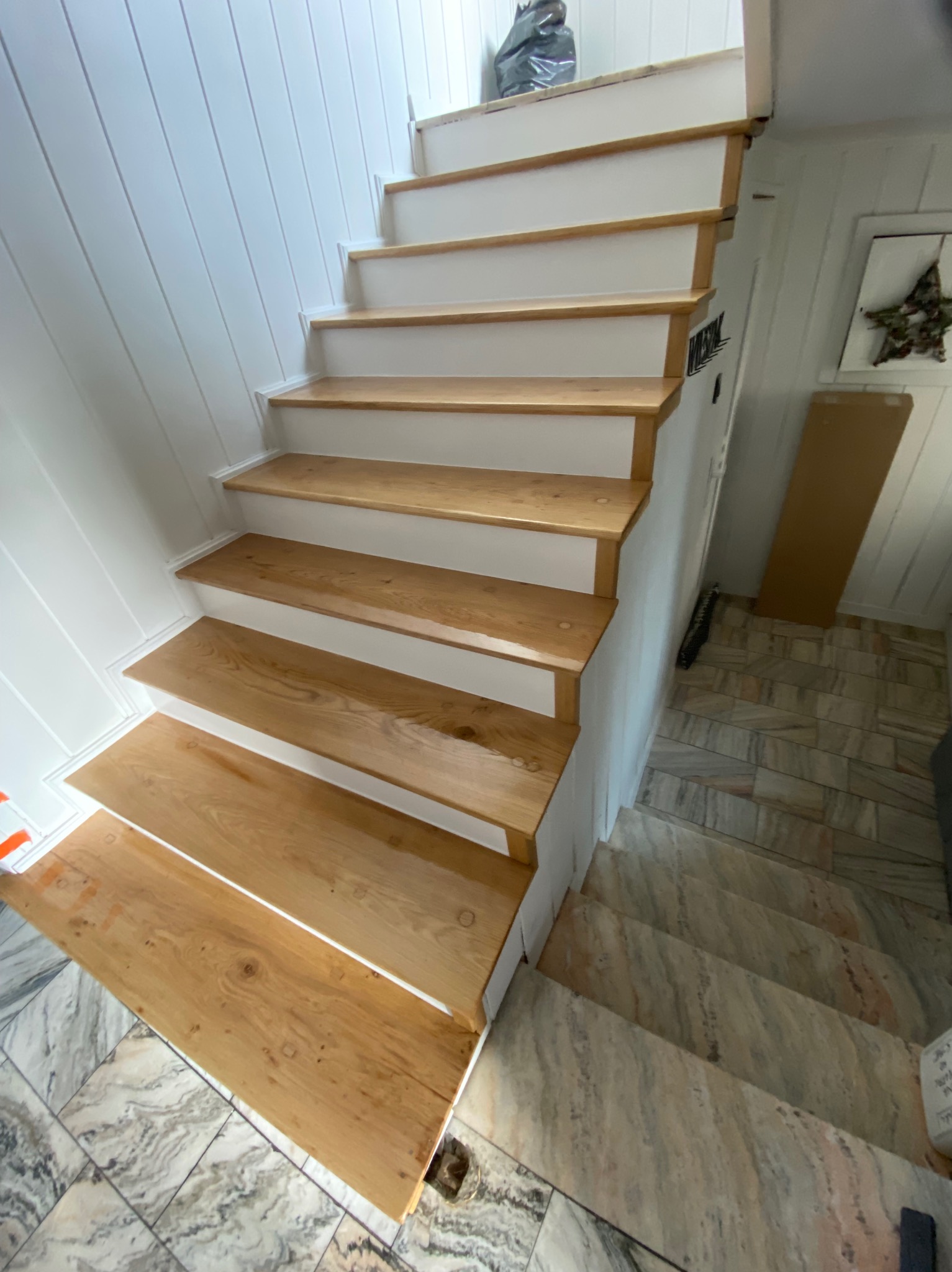 Odnowione drewniane schody z białymi podstopnicami, widoczne sęki na drewnie i marmurowe płytki na podłodze.