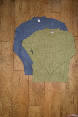 Dwa swetry damskie: niebieski i zielony, leżące na drewnianej podłodze. Zielony sweter ma wyraźny wzór w pionowe prążki.