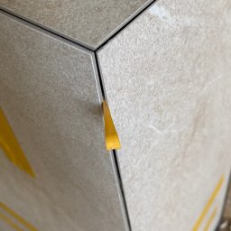 CER-MUR Przemysław Rosik - Detal układania beżowych płytek z użyciem żółtych klinów dystansowych, widoczne fugi.