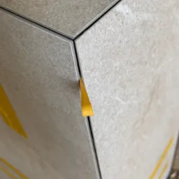 Detal układania beżowych płytek z użyciem ż&oacute;łtych klin&oacute;w dystansowych, widoczne fugi.