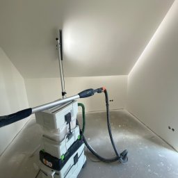 CER-MUR Przemysław Rosik - Szlifierka teleskopowa Festool Planex LHS 225 EQ z odkurzaczem podczas szlifowania sufitu w pomieszczeniu ze skosami, widoczne ślady pyłu na podłodze.