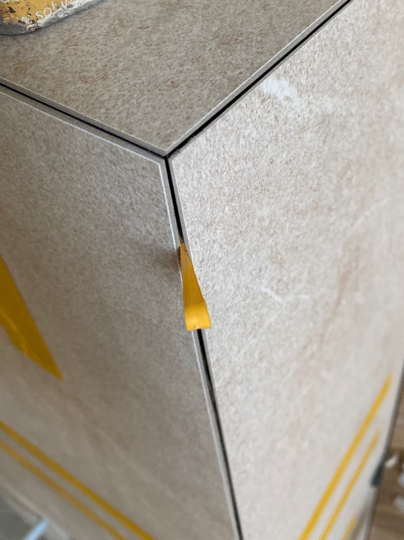 Detal układania beżowych płytek z użyciem żółtych klinów dystansowych, widoczne fugi.