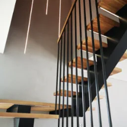 Nowoczesne schody z drewnianymi stopniami podświetlonymi od spodu i czarną metalową balustradą z pionowymi prętami, oświetlenie sufitowe w postaci pionowych linii świetlnych.