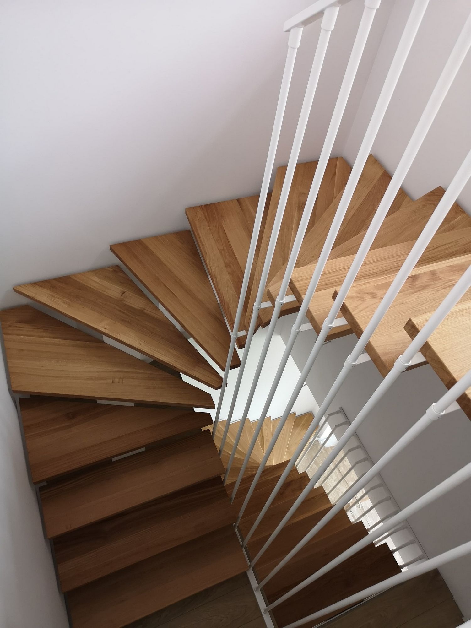 Drewniane schody spiralne z białymi, metalowymi poręczami, widok z góry.