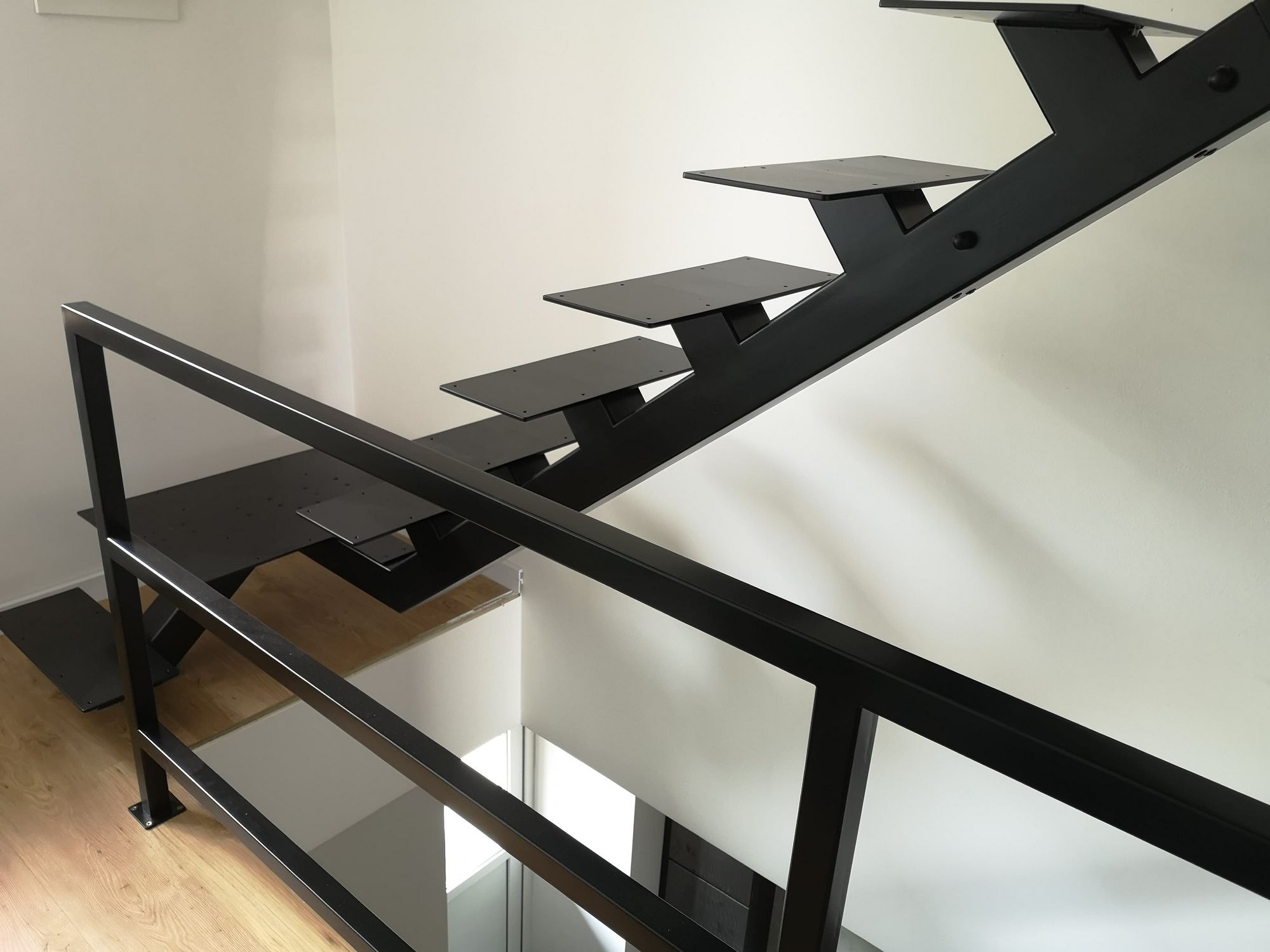 Nowoczesne, czarne schody metalowe z minimalistyczną balustradą, widok od góry, jasne wnętrze.