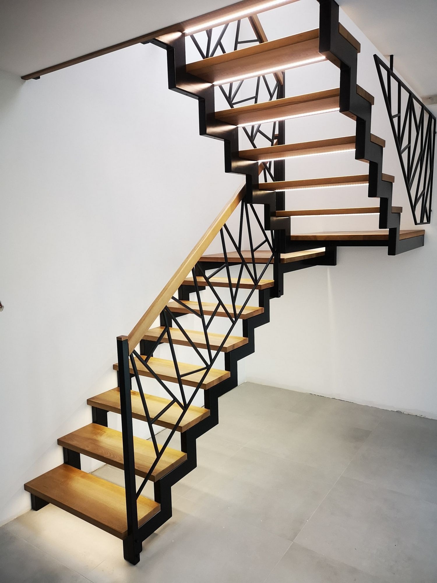 Nowoczesne schody metalowe z drewnianymi stopniami i podświetleniem LED, czarna geometryczna balustrada, jasne wnętrze.