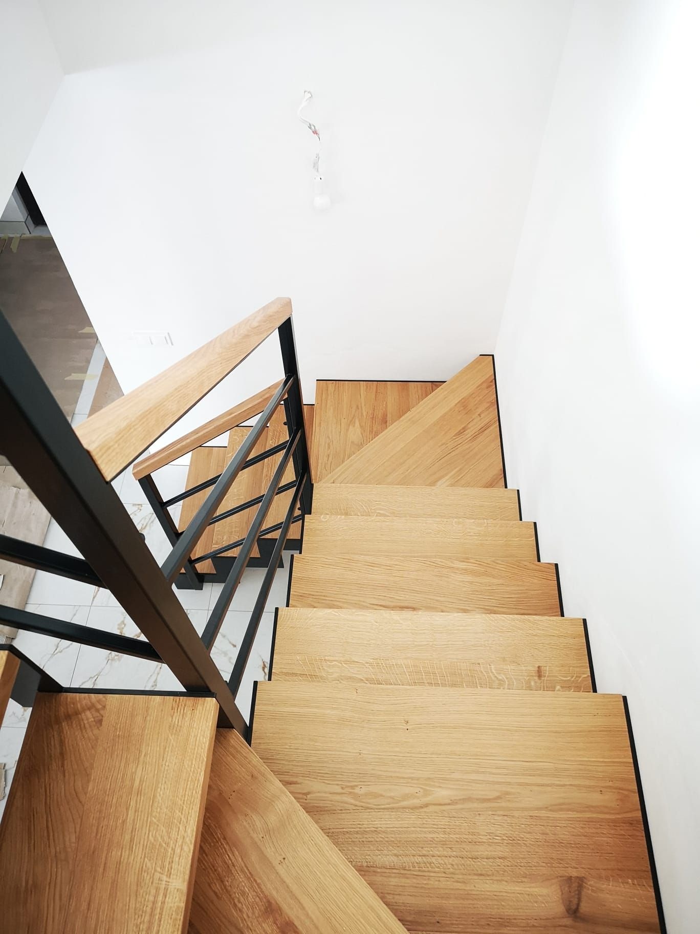 Nowoczesne schody z drewnianymi stopniami i metalową balustradą, widok z góry, minimalistyczne wnętrze z białymi ścianami.