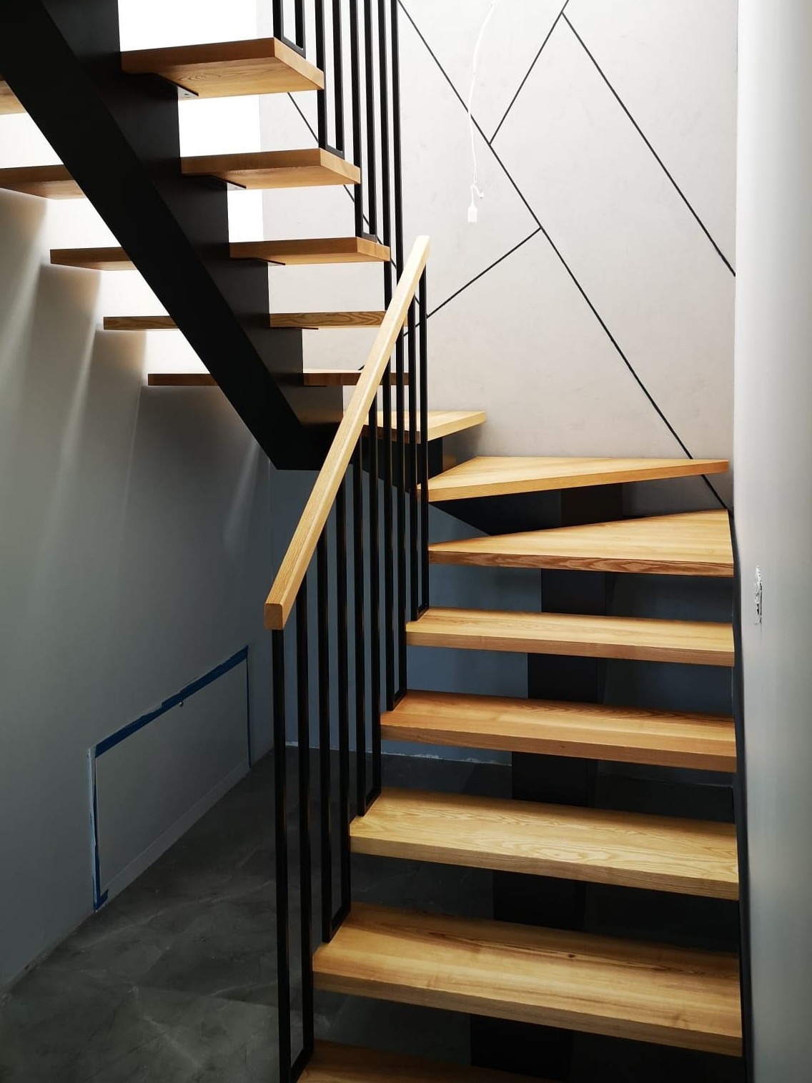 Nowoczesne schody drewniane z czarną metalową konstrukcją i drewnianą poręczą, minimalistyczny design ściany w tle.