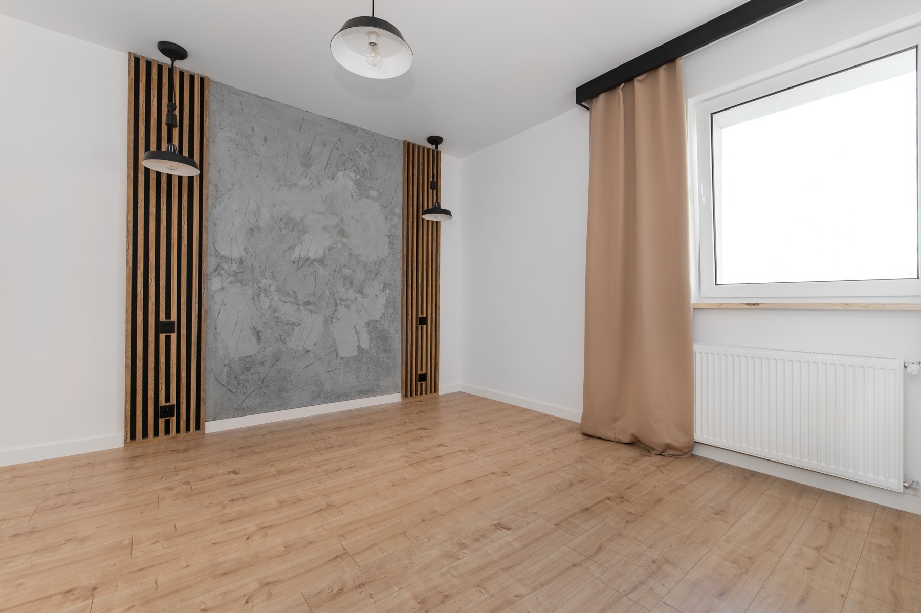Pusty, jasny pokój z panelami ściennymi z listew drewnianych, szarą ścianą z efektem betonu, i lampami wiszącymi. Na podłodze panele podłogowe w odcieniach beżu i brązu. Okno z beżową zasłoną...