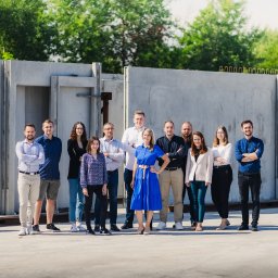 Małro Projekt sp. z o.o. - Grupa pracowników Małro Projekt pozuje na tle prefabrykowanych elementów betonowych, prawdopodobnie fundamentów lub ścian hali.
