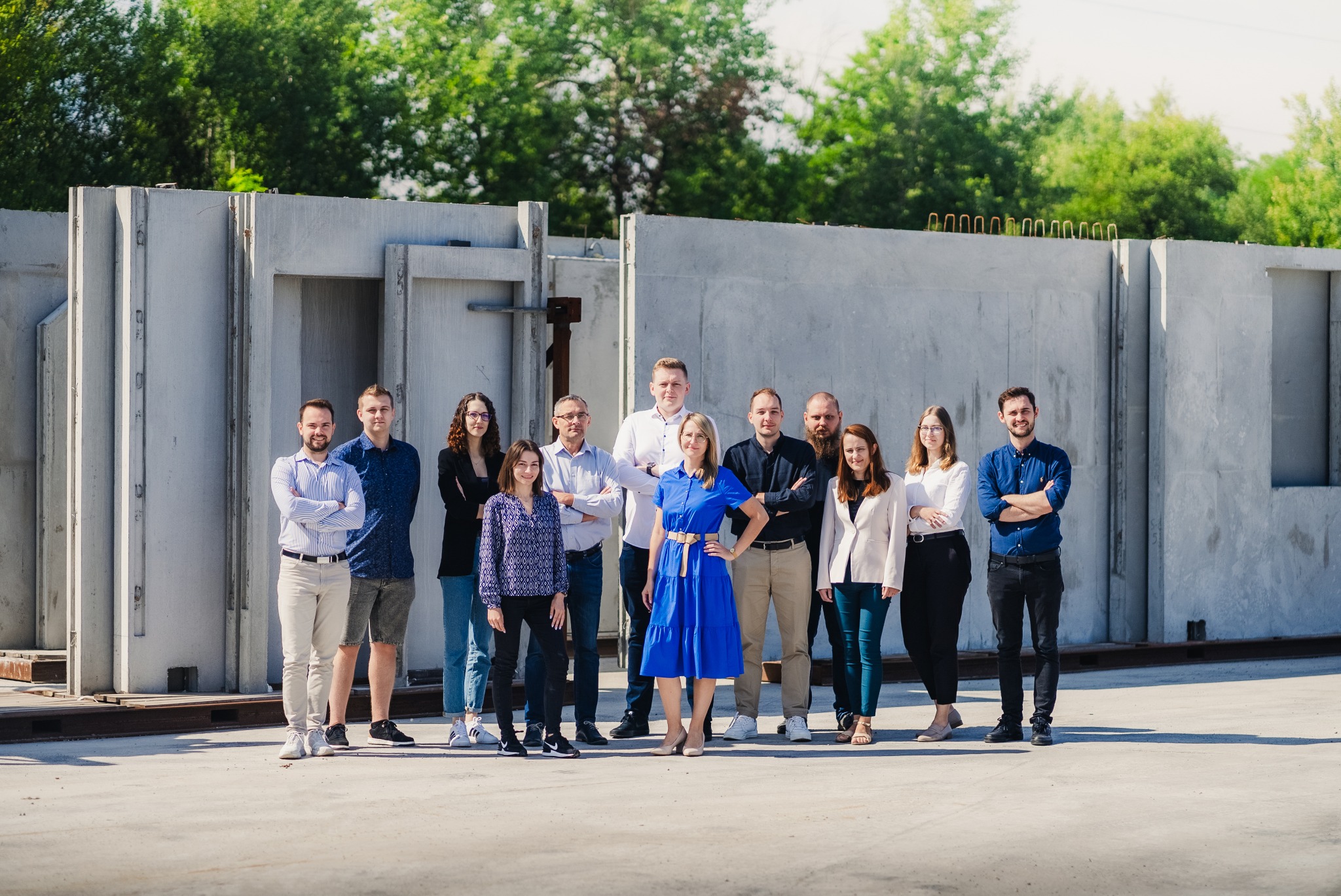 Grupa pracowników Małro Projekt pozuje na tle prefabrykowanych elementów betonowych, prawdopodobnie fundamentów lub ścian hali.