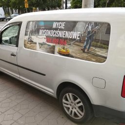 Mangraf Studio - Srebrny samochód dostawczy z reklamą mycia wysokociśnieniowego na bocznych drzwiach, prezentujący osobę czyszczącą powierzchnię za pomocą myjki ciśnieniowej.