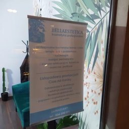 Mangraf Studio - Plakat reklamowy salonu kosmetycznego Bella Estetica z ofertą listopadowej promocji na zabiegi kwasowe, wiszący na tle ściany z motywem tropikalnych liści i zielonego fotela w tle.