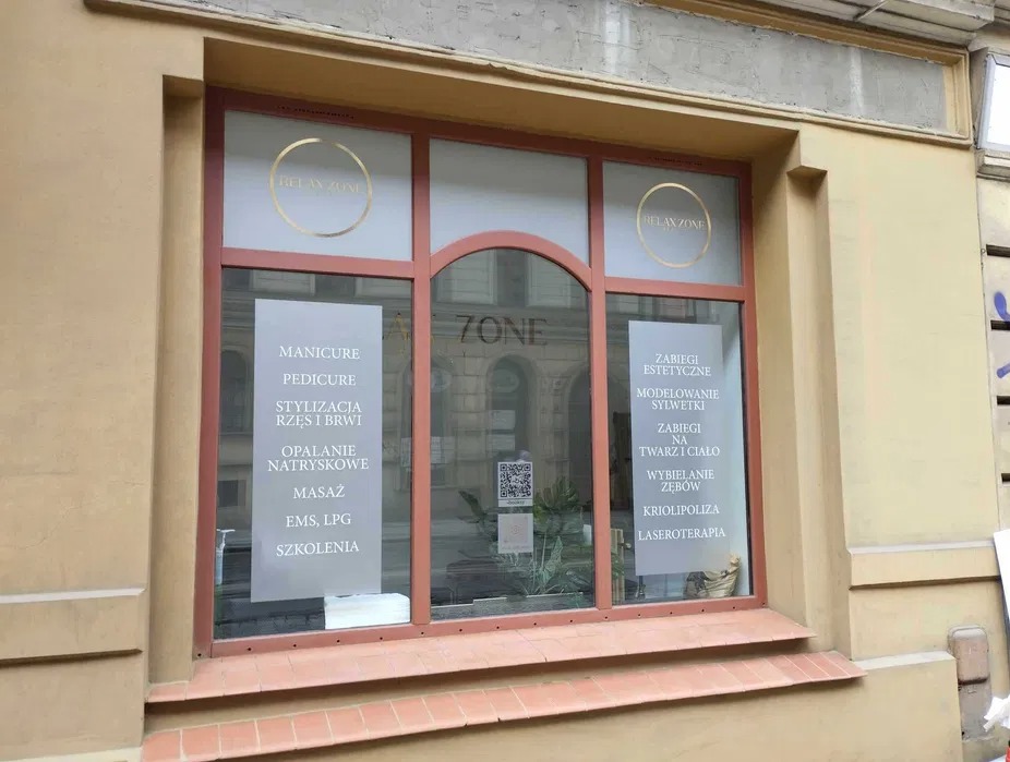 Witryna salonu kosmetycznego z wypisanymi na szybie oferowanymi usługami: manicure, pedicure, stylizacja rzęs i brwi, masaż, zabiegi estetyczne, wybielanie zębów.