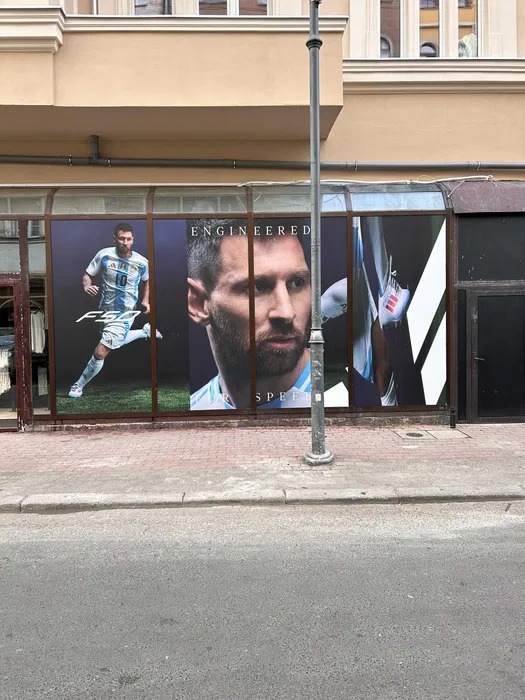 Duże plakaty z wizerunkiem piłkarza Lionela Messiego w witrynie sklepowej na tle ulicy.