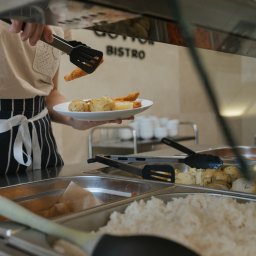 Bistro DoWoli - Osoba w fartuchu nakłada szczypcami smażoną rybę na talerz z ziemniakami z bemaru w barze bistro.