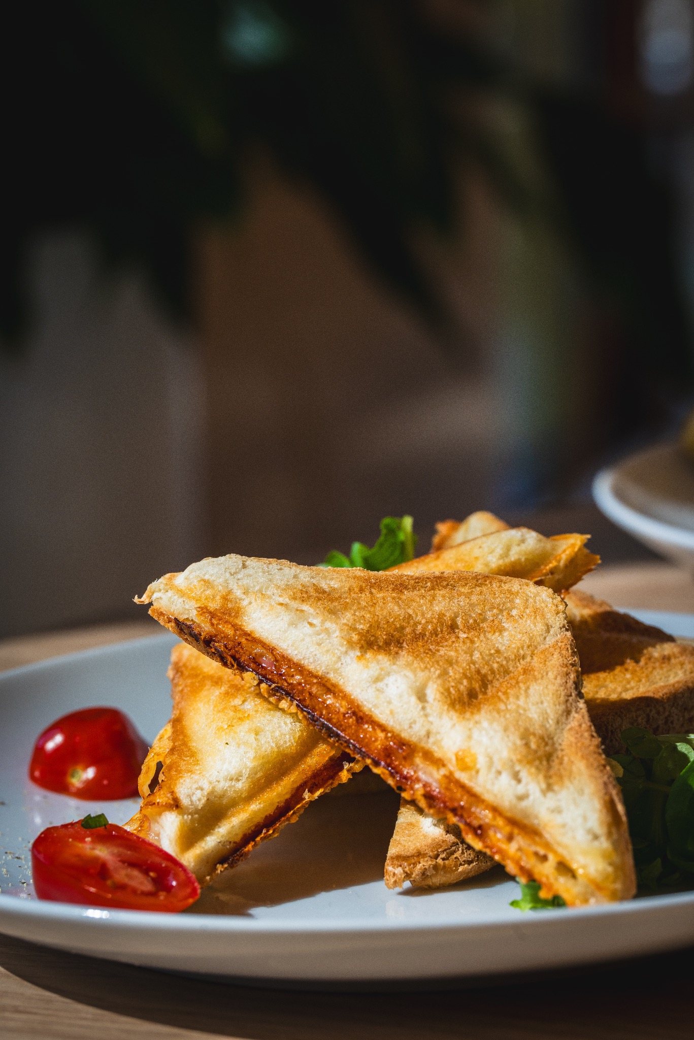 Kremowe tosty z pomidorami i zielonymi listkami na białym talerzu, oświetlone naturalnym światłem, z widocznym wnętrzem z pomidorowym farszem.