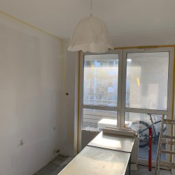 Łukasz Czapiewski - Wnętrze pokoju w trakcie prac wykończeniowych:  ściany przygotowane, zabezpieczone taśmą malarską okna, drabina i stół roboczy.  Widoczny rower za oknem.