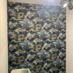 Ściana po tapetowaniu z wzorem drzew na ciemnym tle. Na dole widoczne akcesoria i gniazdko elektryczne. Oświetlenie punktowe na suficie.